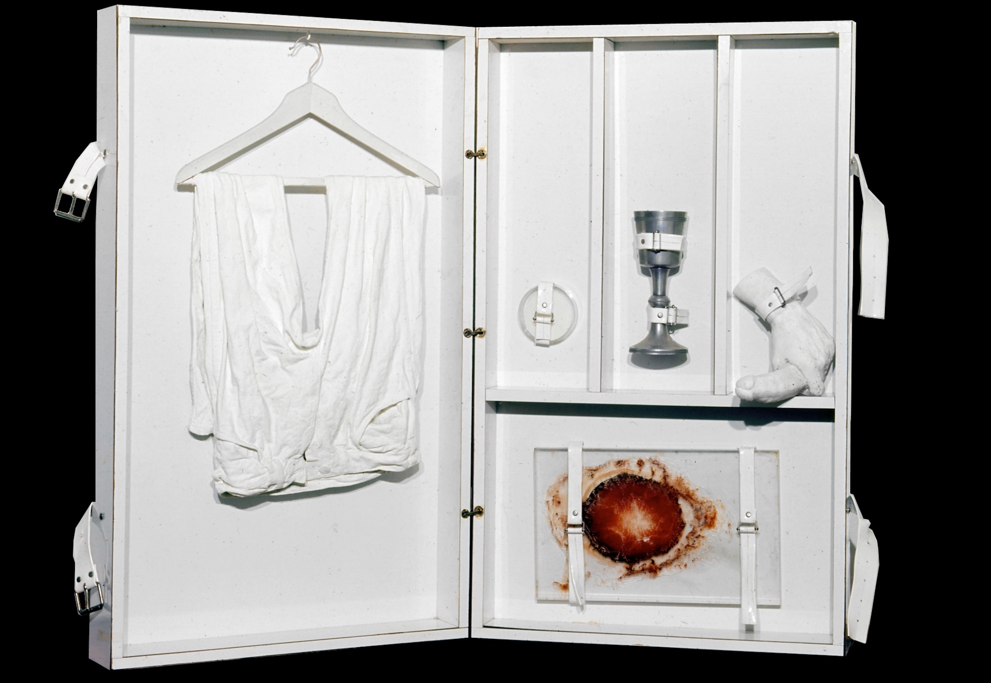 Michel Journiac, Autel portatif, 1969. Hinged cupboard containing long johns with plaster on coat hanger, communion chalice, plaster hand holding penis, paint on paper framed with glass, with straps. Courtesy of Galerie Christophe Gaillard © ADAGP Michel Journiac.